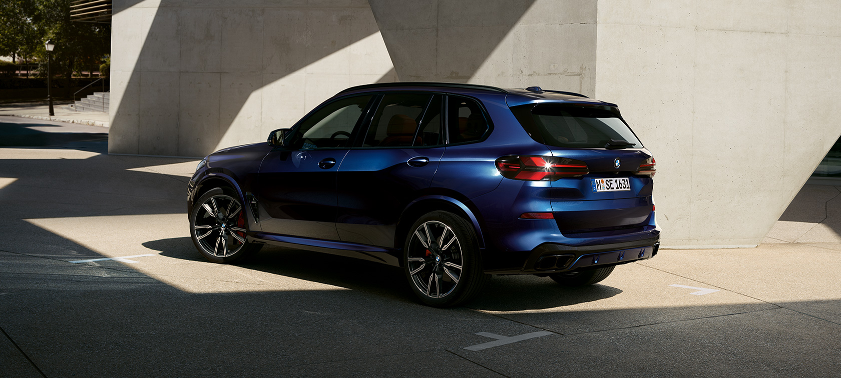 BMW X5 M60i xDrive G05 MP, vue de trois quarts arrière à l’arrêt devant un bâtiment avec incidence de la lumière