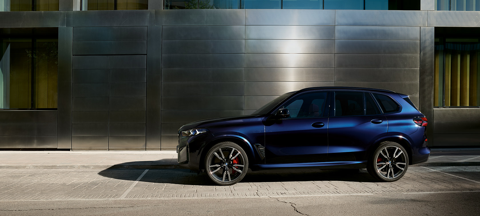 BMW X5 M60i xDrive G05 MP vue de profil à l’arrêt devant un bâtiment